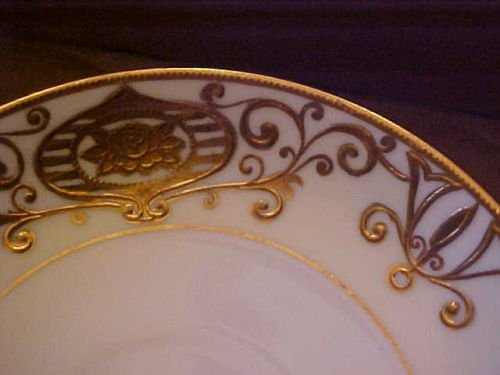 Christmas Ball has a white ground with a yellow border and heavy applied gold enameling in a scrolling pattern with flowers in a ball or bulb form.