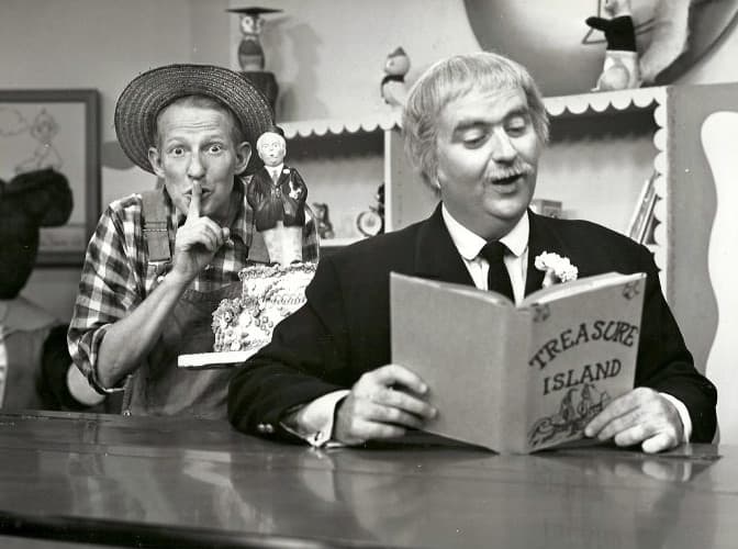 Captain Kangaroo reading from "Treasure Island" while Mr. Green Jeans looks on
