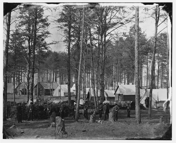 Winter camp at Brandy Station. Note the blankets drying on a line near the tents. Notice the tree stumps in the foreground where trees were felled for building cabins or for use as firewood.