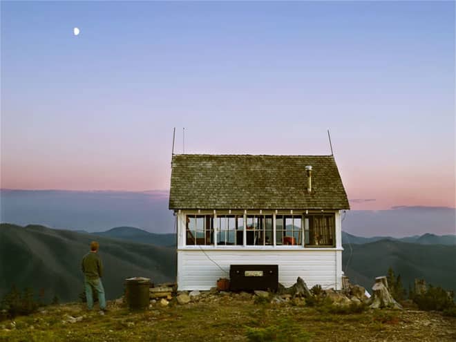 Mountain side home overlooking a mountain range at dusk. Here is a home with a 360 degree window view that shows the surrounding mountain ranges and gives a bigger feel over the home.