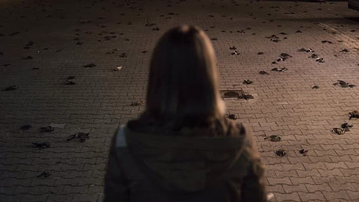 Charlotte Doppler stands outside the police station after a freak electrical surge that leaves the parking lot littered with dead birds in 'Dark' (2017), a Netflix Original Series.