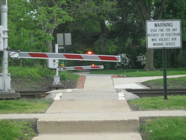 A pedestrian crosswalk near Downtown Hinsdale with the gate down, lights flashing, as the Metra train nears from Chicago