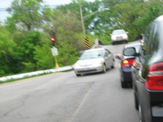 A one-lane street (with cars traveling north while cars traveling south are stopped) overpasses the train tracks just east of Downtown Hinsdale next to the Hinsdale Hospital