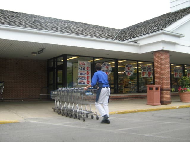 Young man retrieving shopping carts at an independently-owned supermarket - wearing white slacks, dress shirt, and a tie