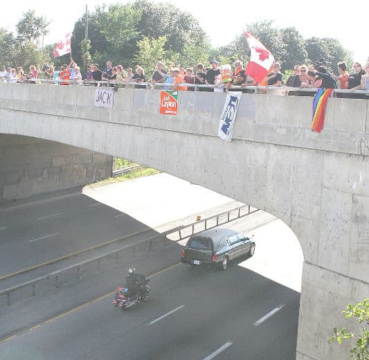 People wave Canadian flags and signs from an overpass as the hearse carrying Jack Layton's body passes along HWY 401 at Kingston, Ont., Thursday, Aug. 25, 2011.