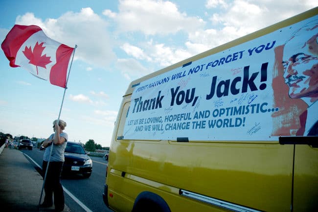 A Canadian flag is waved in Trenton, Ont., while waiting for Jack Layton's funeral motorcade to pass Thursday, Aug. 25, 2011.