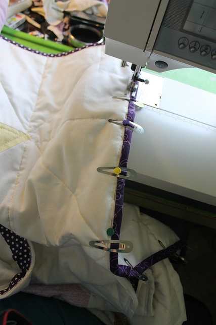 Attaching bias binding to the edge of a quilt to create a bound hem. I like the use of hairclips to hold the binding on.