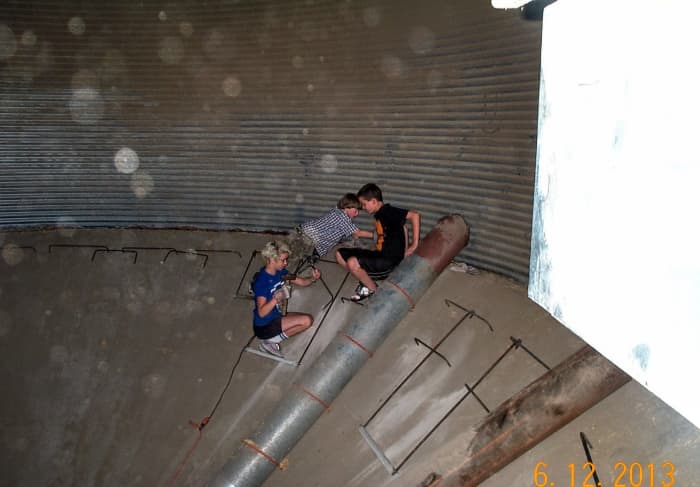 A young work crew in training installs steps made of bent rebar around the perimeter of this pit, using a cement drill to prepare holes in the old concrete.