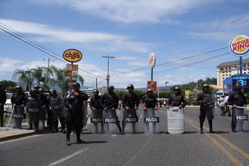 Honduran police officers barricade the street to block of a peaceful, pro-democracy protest march in the capital of Tegucigalpa on February 2010