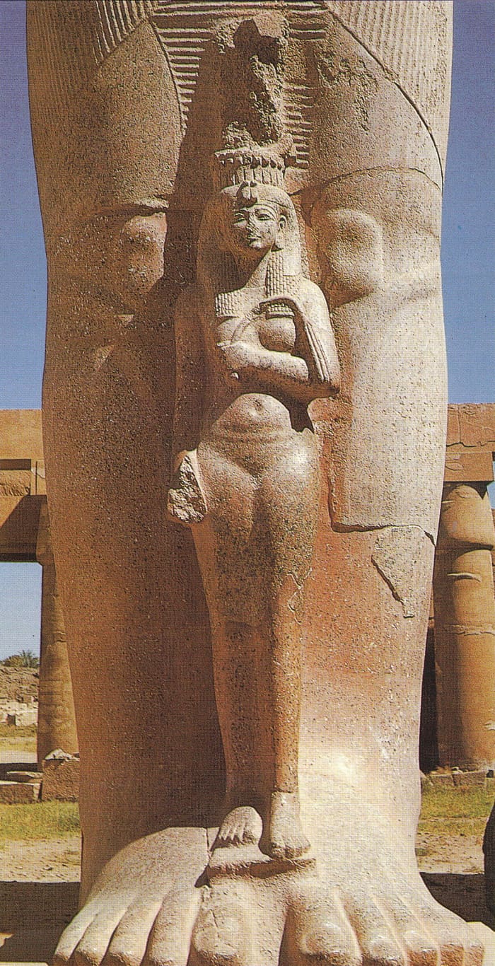 The dimunitive figure of a graceful queen Nefertari standing between the legs of the colossal granite state of Ramesses II in the first courtyard of the temple at Karnak; maybe his daughter Bint-Anath, whose mother was Istnofret