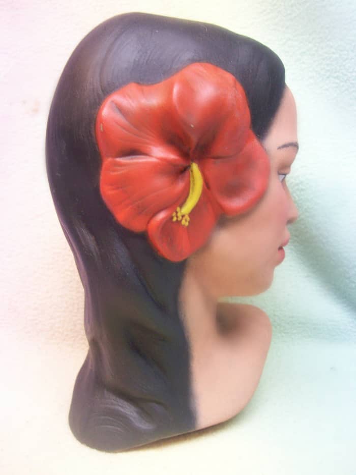 She is a beauty with long black hair adorned with two pretty soft red hibiscus flowers along one side of her head. Her lips are a flesh tone. This is a beautiful example of a handmade, and made in Hawaii Polynesian girl head bust.