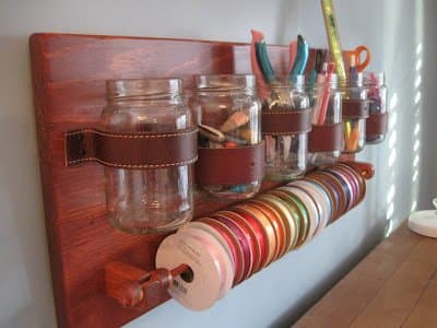 Kristen and her husband created a wall mount craft storage unit with mason type jars, repurposed belts, and a dowel for ribbon.