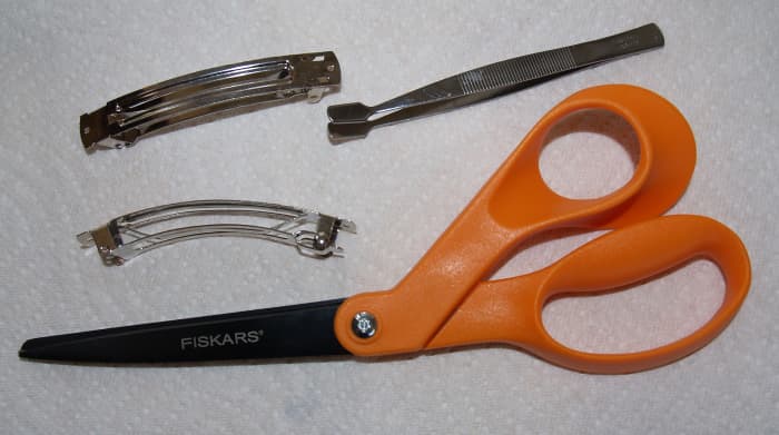Barrette forms, craft tweezers, and scissors with non-stick blades. Barrette forms can be purchased at arts and crafts supply stores. Craft tweezers are helpful in picking up small pieces of tape to add as decorations to the bow.