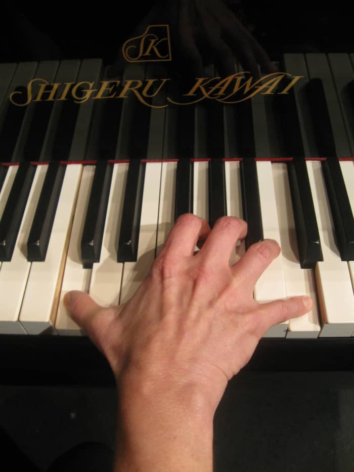 Woman's hand playing an octave on a full size piano. Notice the strain across the knuckles due to the stretching required to reach the notes.