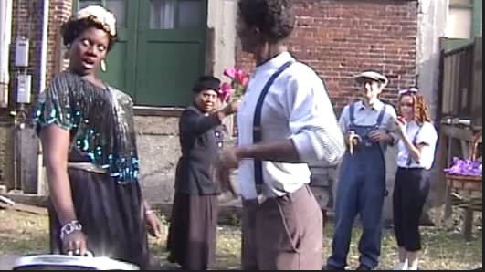 This reenactment portrays Ma Rainey arguing with and giving a humiliating thrashing, with the lid of a garbage can, to a man who allegedly cheated her in a dice game. A "flower lady" and other Beale Streeters look on in amazement.
