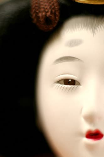 Detail of Gofun doll face shows individual expression with traditional makeup. Tiny brushes are used to create individual hairs of eyelashes and brows.
