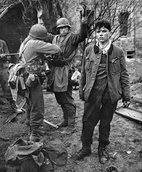U S soldier frisks German for hidden weapons, another dishevelled POW stands nearside looking sorry for himself - these are just about school leaving age, (older than some who 'defended' Berlin against the Russians)