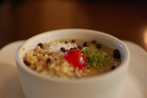 A small bowl of asure topped with grated pistachios, nuts, raisins & other currants.