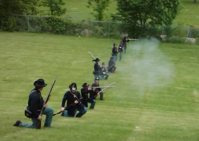 Living Historians Load and Fire during a reenactment. The soldier, second from left, is about to load his musket from the Kneeling Stance. His musket was brought back on his right side, rammer-side up, and in this position he will load the firearm
