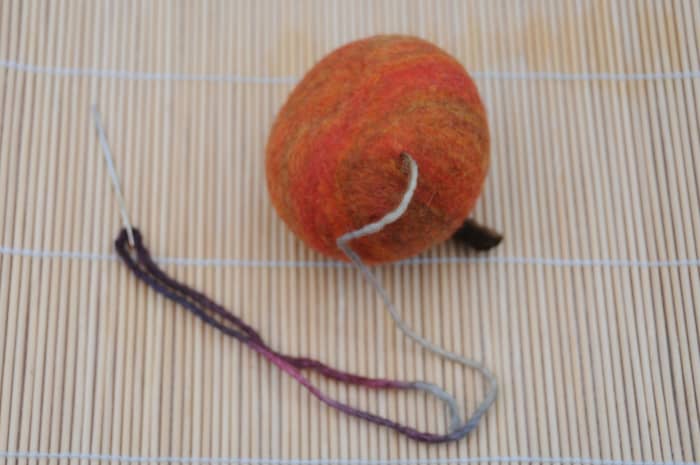 Take the needle right through the hole and then insert it back into the apple and cut the yarn.
