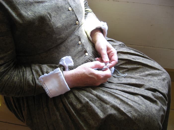 Here's a woman is making lace. You can see examples of it on the cuffs of her dress. This dress appears more formal than that worn by women in the more humble homes. The dress fabric is probably store-bought.