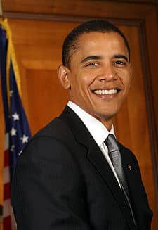 He has short, black hair, sparkling brown eyes and a broad, friendly smile. He is wearing a dark suit and tie. He appears to be fit and trim. He looks like an intelligent, competent man.