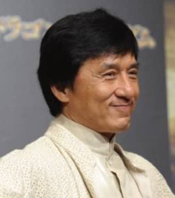 He has neatly cut short black hair, a pleasant smile, and friendly eyes. He appears to be quite fit. He is wearing a white traditional Chinese suit. He seems to be a confident man.