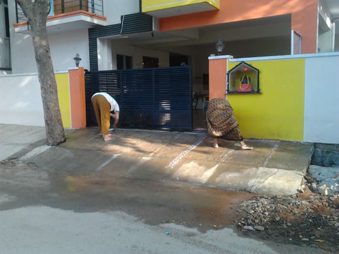A mother and daughter beginning to draw an elaborate rangoli in front of their house for a festival.