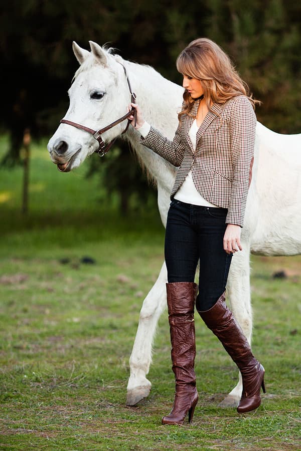 High Fashion Equestrian Style - Beautiful Model in Riding Pants, Boots and Gloves Leading a White Horse