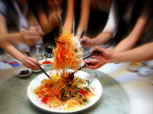 Serving yee sang: Using chopsticks, the ingredients are mixed and tossed as high as possible