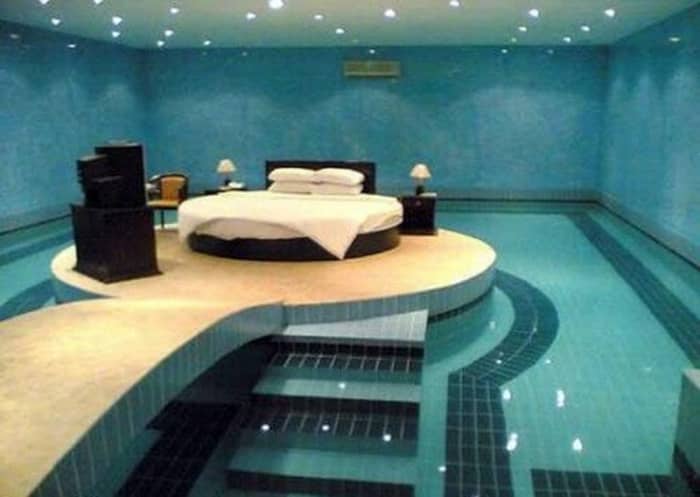 a round swimming pool surrounds the bed in this extreme bedroom suite complete with night stands and table lamps and a dresser