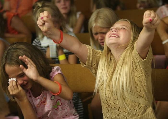 Lacey Johnson, 9, left, and Jasmine Anderson, 9, right, and Jaimie Brown, 10, in the center background, weep and raise their hands, after listening to a gospel presentation by Jason Mansur, a children's minister from Harvestime Church of Eau Claire,