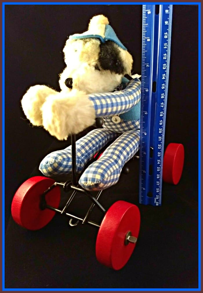 The dog looks like a Dalmatian (he has spots) and black and white ears. He has a red felt tongue and embroidered black mouth and nose. He is wearing blue and white checkered overalls, and a blue felt shirt with blue and white checkered sleeves.
