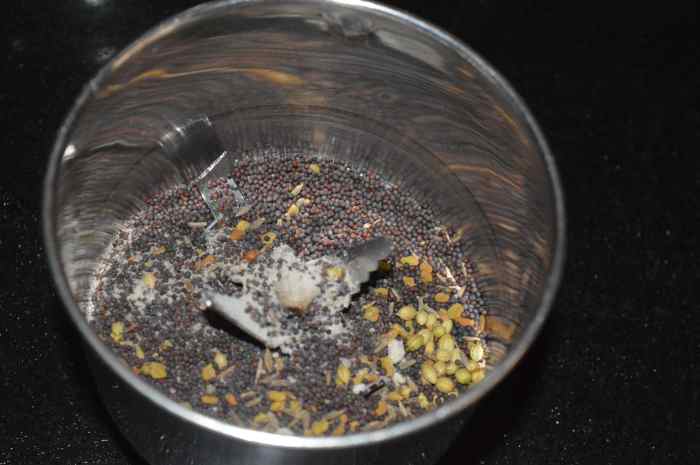 Step two: Heat the ingredients for making garlic pickle as per instructions. Add warmed mustard seeds, fenugreek seeds, cumin seeds, coriander seeds, and hing powder to a mixer. Grind them to get a fine powder.