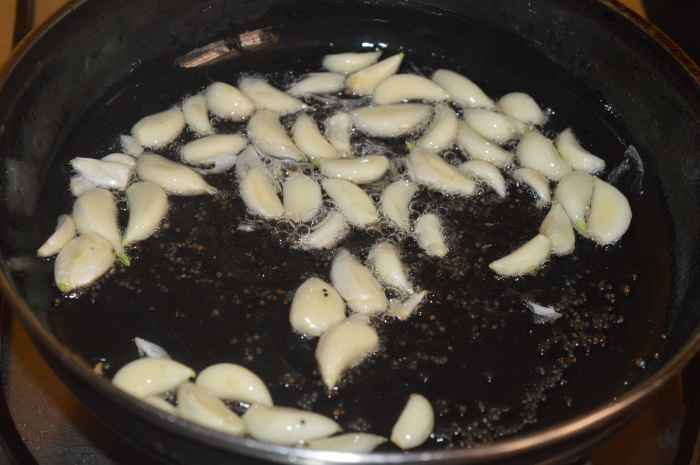Step three: Heat oil in a deep bottomed pan. Add some mustard seeds. Let them crackle. Add peeled garlic cloves. Saute on a low fire. Saute it until the garlic turns golden brown.