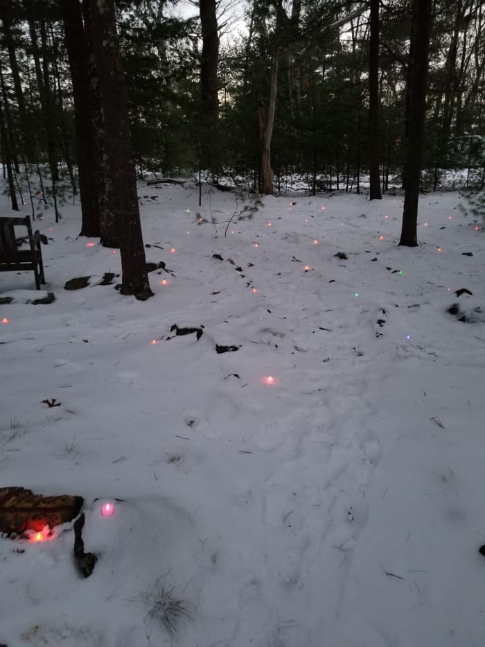 Footprints on the snowy wooded labyrinth path lit with rainbow lights for the Winter Solstice in New England. Dusk is a magical time to walk a labyrinth. It is the time of transition between afternoon and evening.