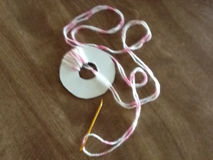Thread tapestry needle with yarn and pull it through the doughnut hole, in and out ..over and over.