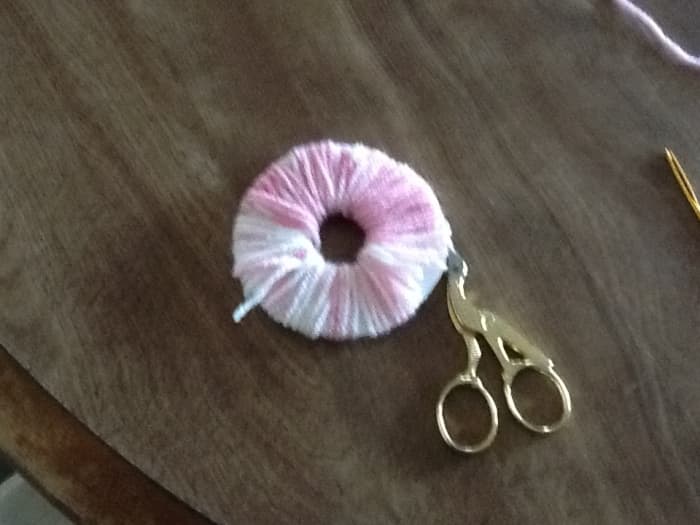 With scissors cut the yarn carefully around the out side edge. Your scissor blade should go between the two pieces of cardboard.