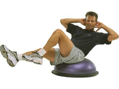 Man in black t-shirt and tan short performing sit-ups while sitting on top of a purple bosu balance ball