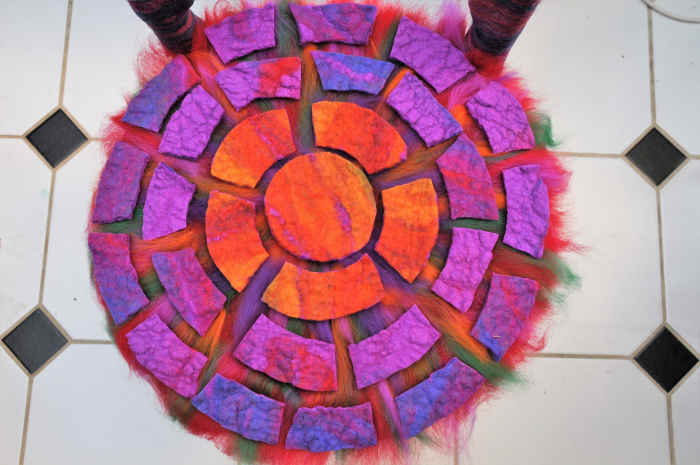 Covering the seating area with a fine layer of contrasting merino wool fibers and then a layer of pre-felted cut pieces.