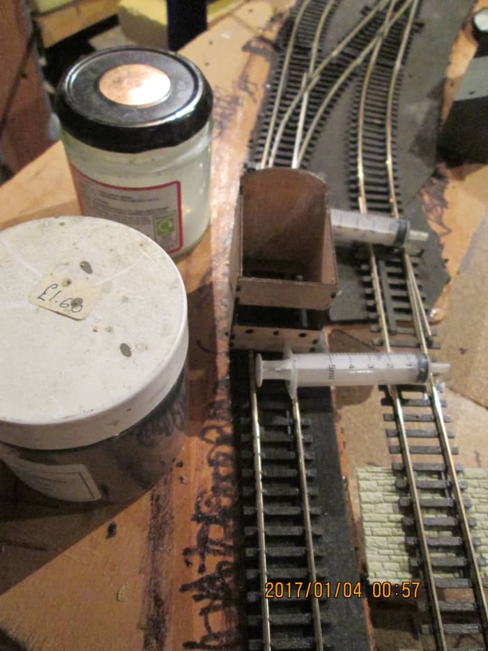 The tools for the ballasting job: large syringes suitable for pushing through dilated PVA/wood glue solution + washing-up liquid, jar of ballast (ash) and Poppy's Woodtech box with its 'chute' and lateral slot to allow an even flow of ballast