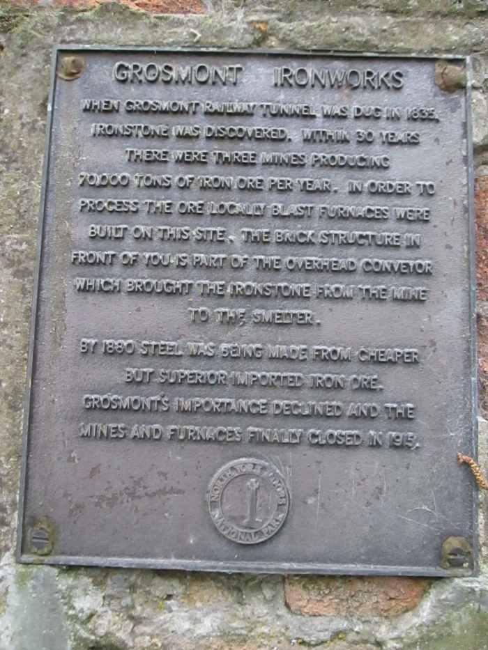The iron works, commemorated by this plaque, opened late1830s to process ironstone mined nearby in Eskdale after iron was found during digging the original tunnel bore. The site is north of the line to Whitby