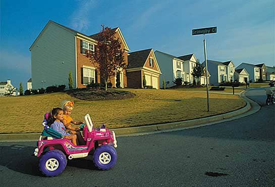 Two girls enjoy the safe and quiet serenity of their neighborhood- taking their Barbie Jeep out for a spin.