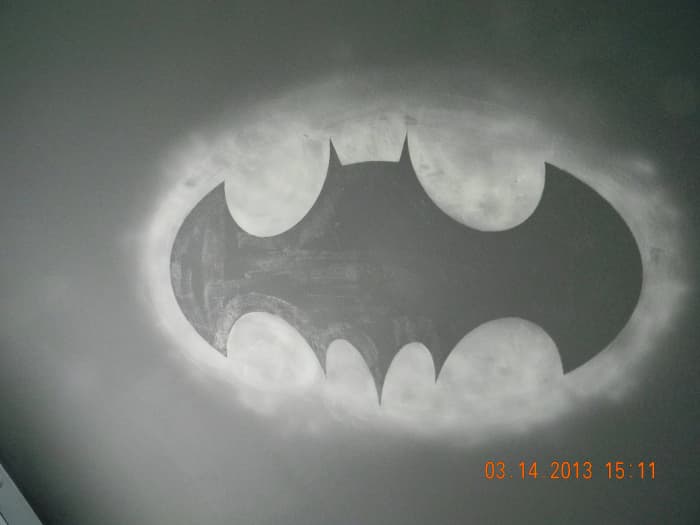 This is the glow in the dark Bat Symbol on the ceiling of the Batman themed bedroom. The outlying oval glows around the black symbol giving the illusion of an actual light being shown on the clouds above. It was produced with Krylon Glowz spray.
