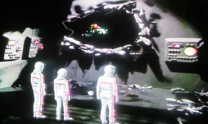 Oro's Ship taking off from the Starlost and Heading back to his home world. Devon, Rachel and Garth are in their spacesuits looking out of the damaged hole Oro made to the Ark when he crashed into it.