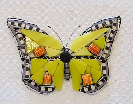 Edged in plate rim. Yellow stained glass, black faceted bead cut in half and hematite bead body. Orange dichroic glass accents. Will be grouted with black grout.