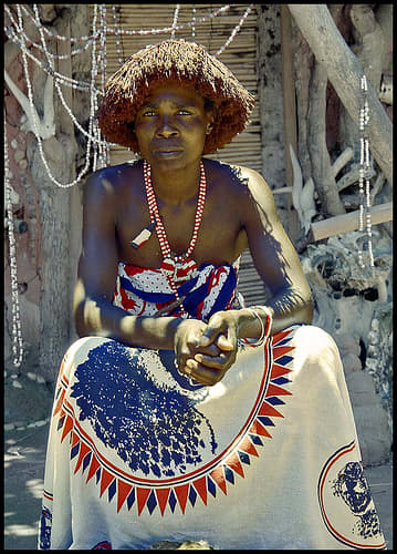 A Shangaan man sitting next to her hud and wearing his hair the traditionally Shangaan way, and a cloth and beads