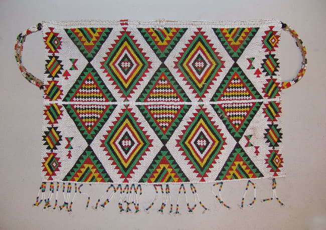Zulu beaded apron made with tiny glass beadsDazzling geometric designs were created by use of the brick stitch. Triangles in this apron are recorded to represent traditional Zulu Shields