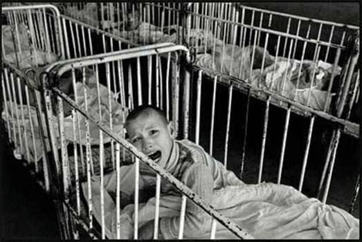 A Romanian orphan in the early 1990s, surrounded by other orphans. "Babies who don't get attention when they cry learn to stop crying."