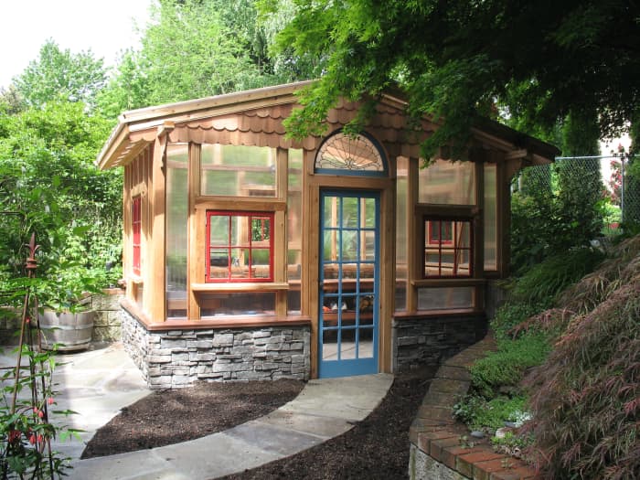 beautiful wood garden shed with walls of windows including arched window lights and a stone foundation